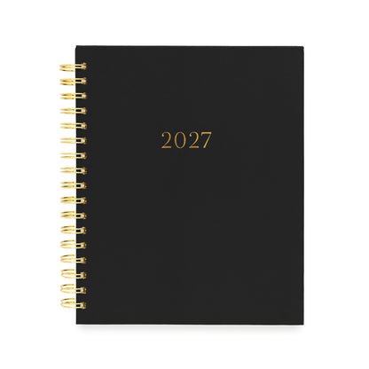 A black 2027 spiral-bound planner with gold lettering and gold wire binding with gold foil '2027' numbers