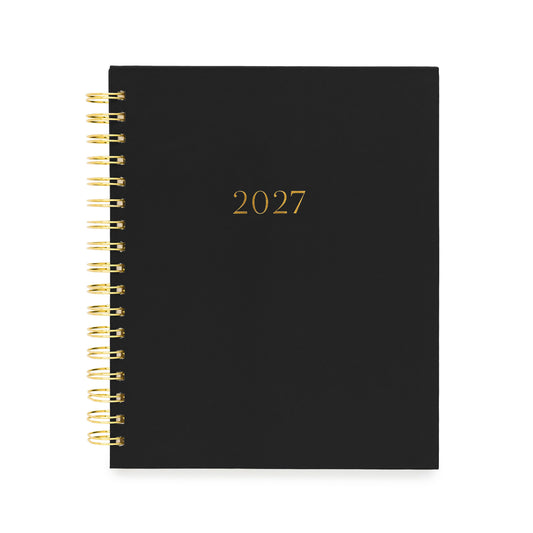 A black 2027 spiral-bound planner with gold lettering and gold wire binding with gold foil '2027' numbers