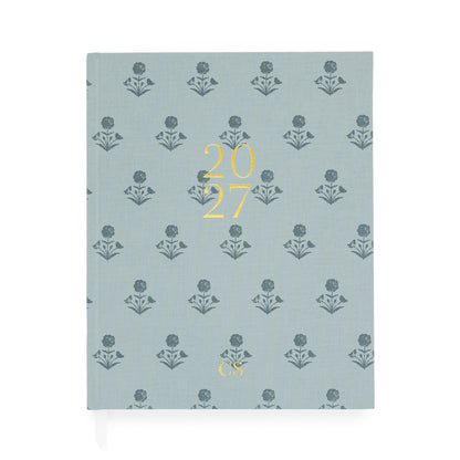 A hardcover planner with a dusty blue fabric cover featuring a repeating dark blue floral pattern and gold foil text reading '2027' and 'CS', shown on a clean white background.