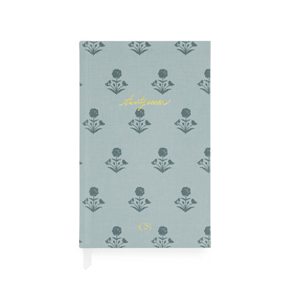 A hardcover 2027 agenda with a dusty blue fabric cover featuring a repeating dark blue floral pattern and gold foil accents, including the script title 'twenty-seven' and the initials 'CS'.