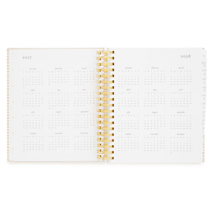 An open spiral-bound planner showing the years 2027 and 2028 with monthly grids and a gold spiral in the middle
