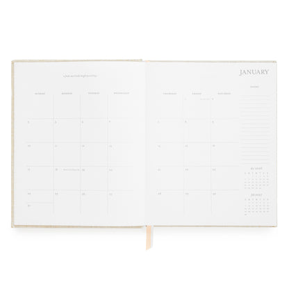 An open planner showing blank monthly calendar pages for January with light pink and white ribbon markers and notes section on the side