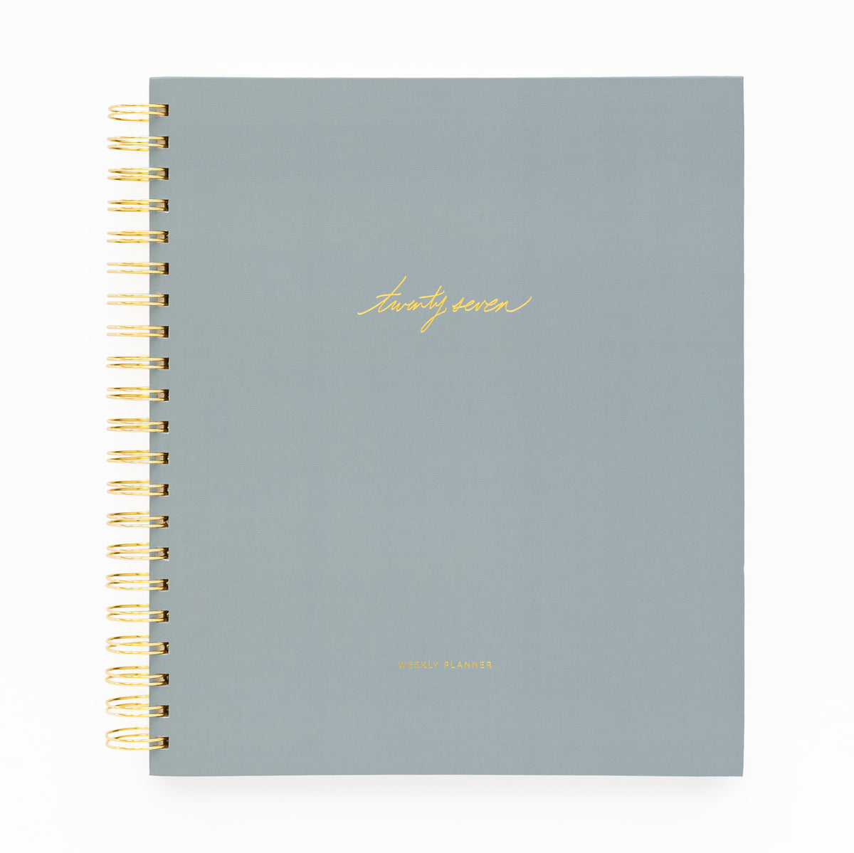 A 2027 spiral-bound planner with a matte slate blue cover and gold foil lettering with 'twenty-seven' and 'weekly planner' stamped on cover with a gold coil spiral