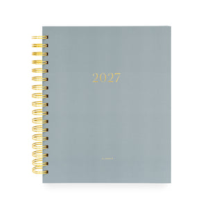 A 2027 spiral-bound planner with a matte slate blue cover and gold foil lettering with '2027' and 'planner' stamped on cover with a gold coil spiral