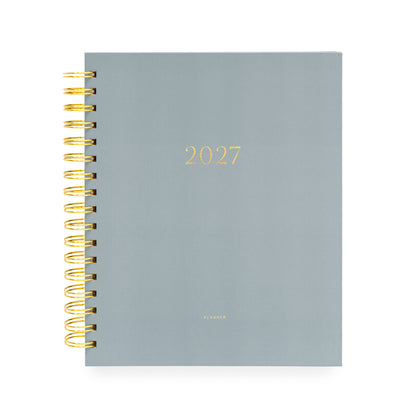 A 2027 spiral-bound planner with a matte slate blue cover and gold foil lettering with '2027' and 'planner' stamped on cover with a gold coil spiral
