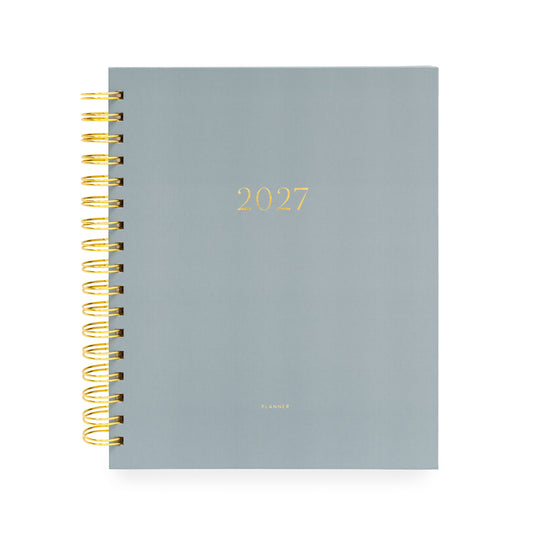 A 2027 spiral-bound planner with a matte slate blue cover and gold foil lettering with '2027' and 'planner' stamped on cover with a gold coil spiral