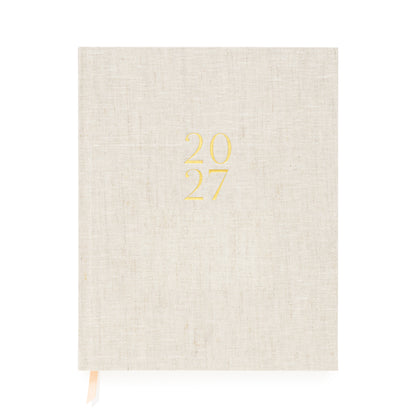 A flax linen fabric bound 2027 planner with gold foil '2027' on the cover and pink and white ribbon markers