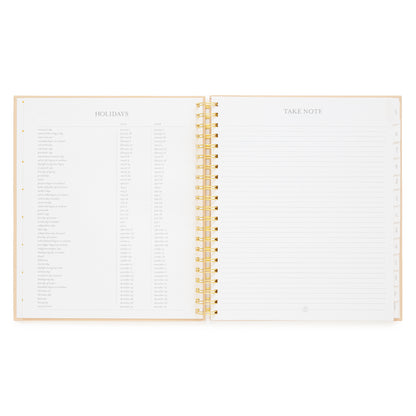 An open spiral-bound planner with gold-spiral, showing two white interior pages. The left page is headed 'HOLIDAYS' with a list of holidays and dates for 2027 and 2028, and the right page is headed 'TAKE NOTE' with lined writing space.