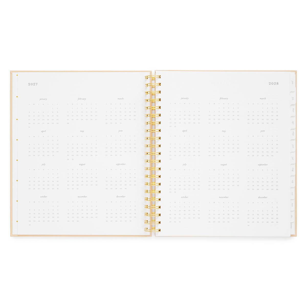 An open spiral-bound planner showing monthly calendar pages for 2027 and 2028, with a light pink cover and gold spiral binding