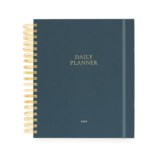 A navy blue daily planner with gold wire binding on the left and gold foil text reading 'DAILY PLANNER' and '2027' on the front cover
