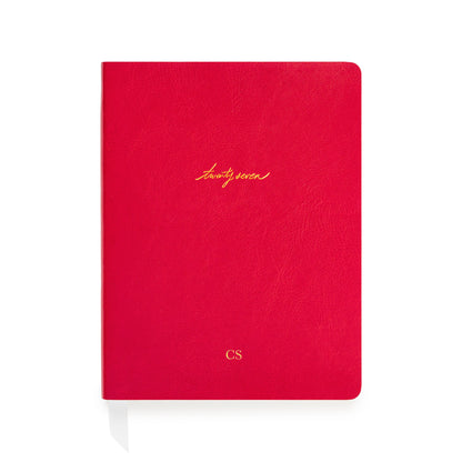 A red textured leather-bound planner with gold foil script reading 'twenty seven' and a small gold 'CS' monogram near the bottom, shown on a white background.