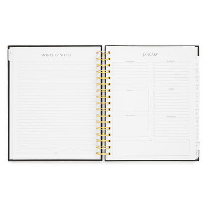 An open spiral-bound planner with white pages, showing a monthly notes page on the left and a January calendar layout on the right with goal setting prompts
