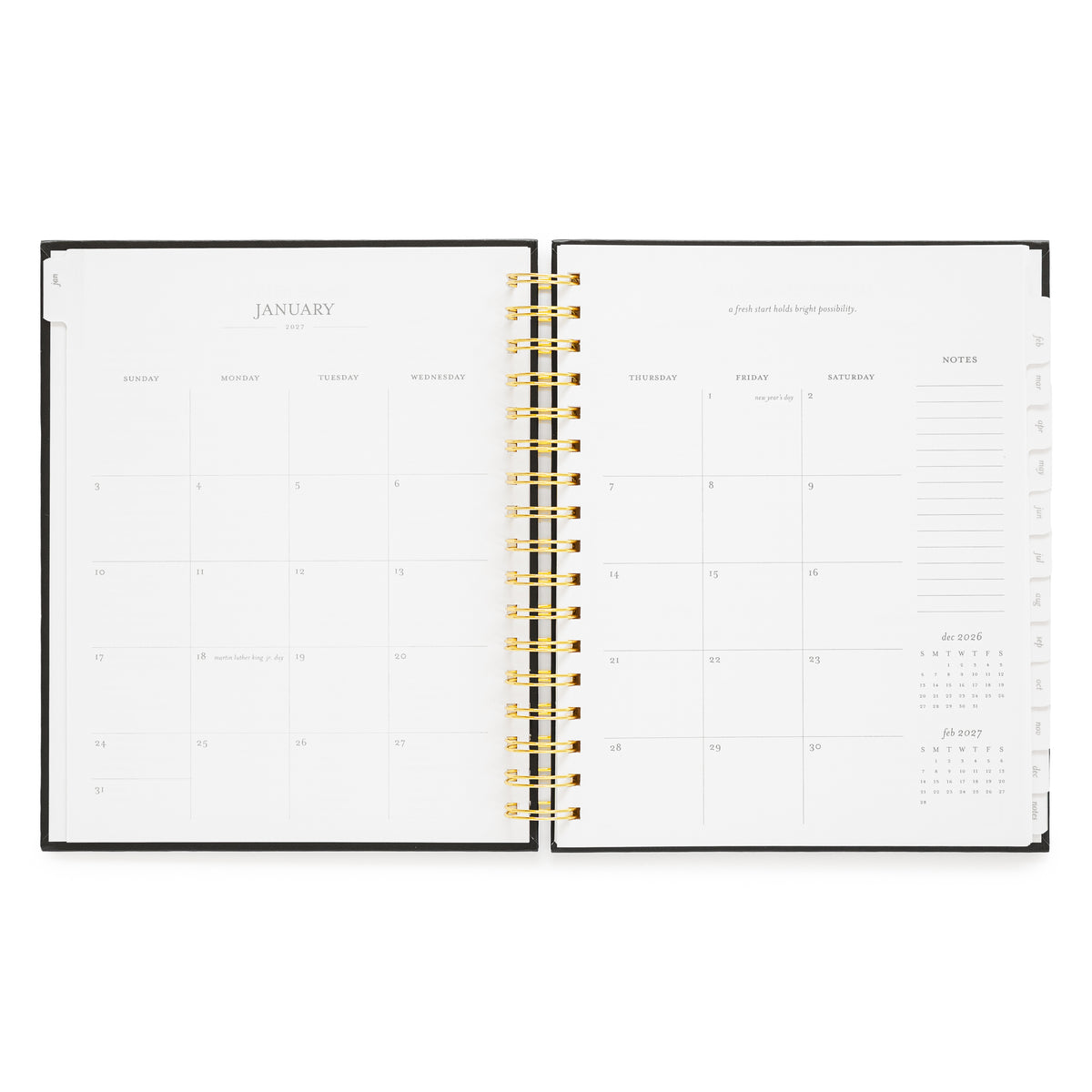 An open weekly planner with a black cover and gold spiral binding, showing the January monthly calendar page with a box for each day of the month, an inspirational quote, and notes