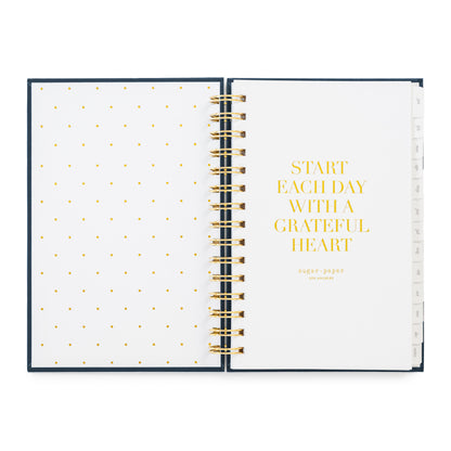 An open spiral-bound planner with white pages, gold polka dots on the left page, and gold text reading 'START EACH DAY WITH A GRATEFUL HEART' on the right page in gold foil
