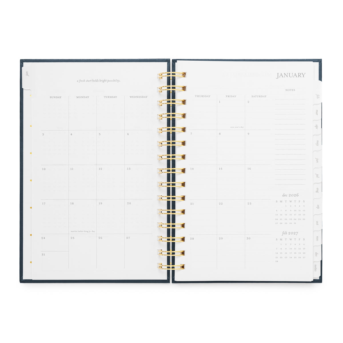 An open spiral-bound planner with a dark navy cover visible. The layout is a January 2027 calendar with spaces for each day of the month, an inspirational quote, and a notes section on the right
