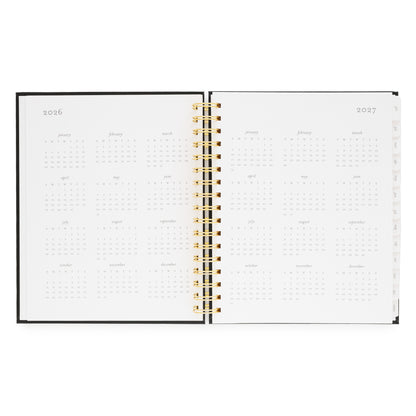 Open spiral planner with 2026 and 2027 calendar months with a gold spiral binding
