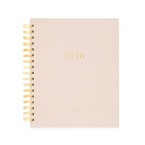 Blush pink planner with '2026' printed on it, featuring a gold spiral binding.