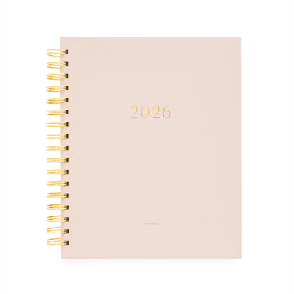 Blush pink planner with '2026' printed on it, featuring a gold spiral binding.