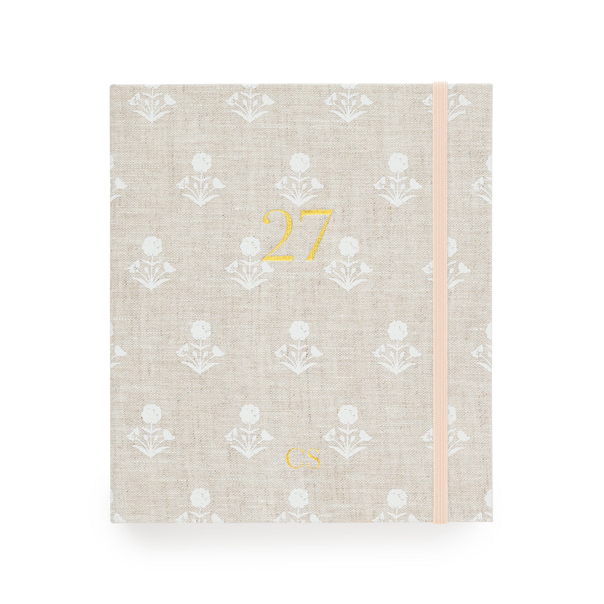 A 2027 fabric planner  with a beige linen cover, featuring a white floral pattern, a gold foil '27' on the front, and a pale pink elastic closure band with "CS' in the bottom center