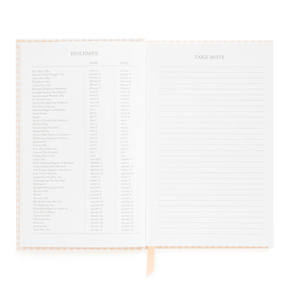 Open small bound agenda with 2026 + 2027 holidays and take note section with ruled lines