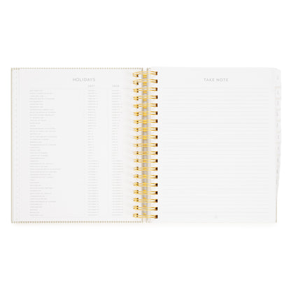 An open spiral-bound planner with gold wire binding, showing ruled lines on the right with 'take note' and printed tables on the left page for '2027' + '2028' holidays