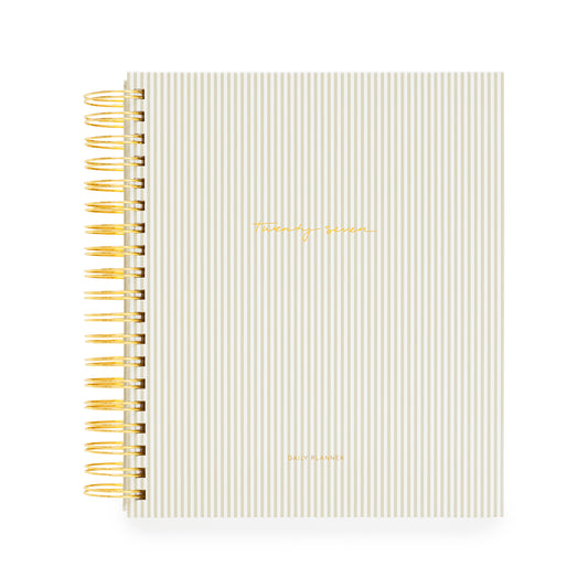 A beige and white stripe spiral bound planner with a gold coil and 'twenty-seven' and 'daily planner' stamped in gold foil on the cover