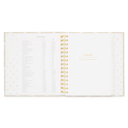 An open spiral-bound planner showing the January title page with a holiday list for 2027 + 2028 holidays on the left and gold spiral in the middle