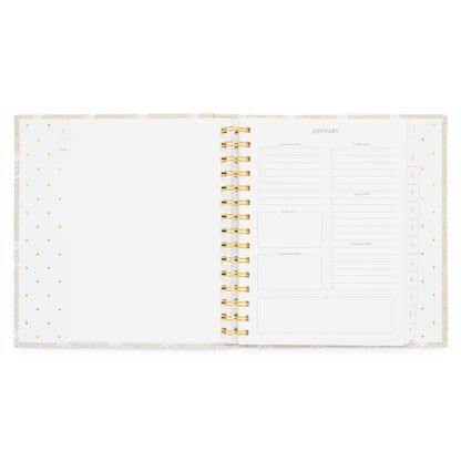 An open fabric spiral-bound planner with white pages with january monthly goal prompts on the right side
