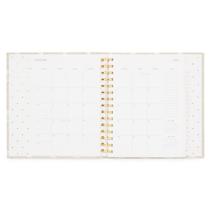 An open spiral-bound planner showing a January 2027 calendar monthly spread with gold spiral in the middle