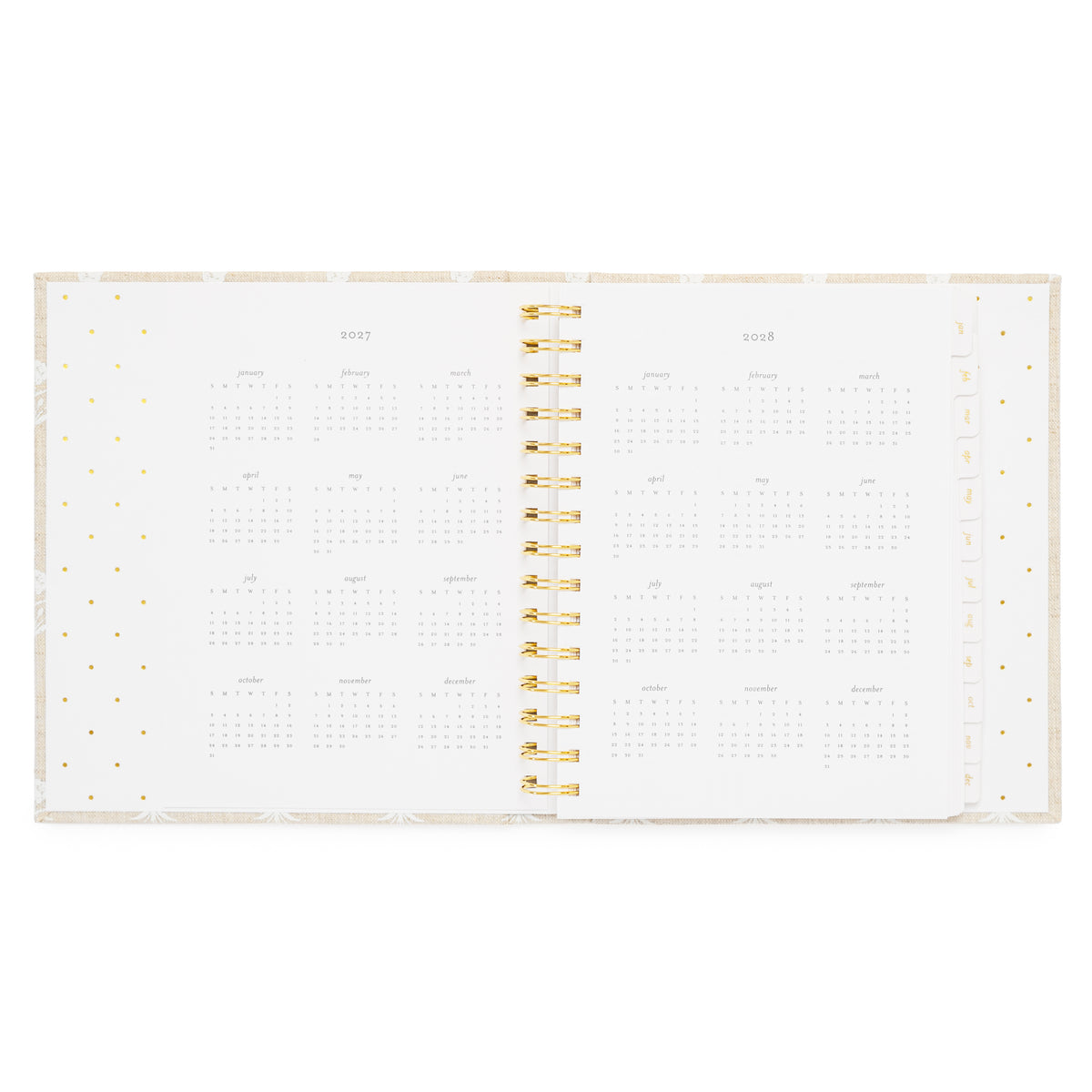 An open fabric spiral-bound planner showing the year 2027 + 2028 with monthly grids on white pages with a gold spiral in the middle