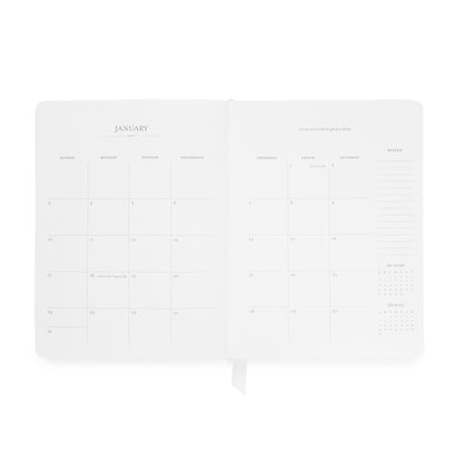 An open white planner showing the January page spread with minimalist columns for daily planning, a notes section on the right side, and a quote at the top