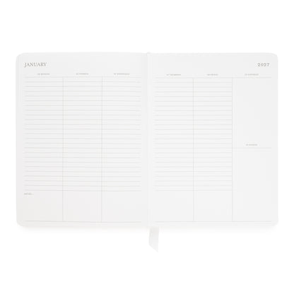 An open planner showing January 2027 with lined daily sections for the week and a ribbon bookmark hanging from the bottom center