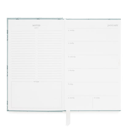 An open planner with a white interior showing lined note pages on the left and a January weekly layout on the right