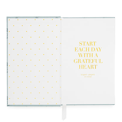 An open planner on a white background, showing a white left page with small gold foil polka dots and a white right page with the gold text 'START EACH DAY WITH A GRATEFUL HEART' and the brand name 'sugar_paper' below.