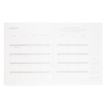 An open planner showing two white pages with minimalist February calendar layouts and writing sections, notes on the side, a monthly focus of 'daily space' and january and march month overview