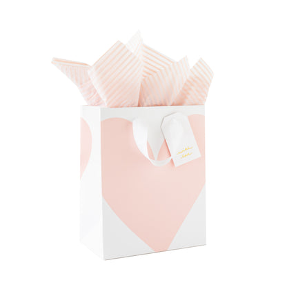 Gift bag with pink heart on a white background with pink stripe tissue paper and a white gift tag with gold foil 'with love'