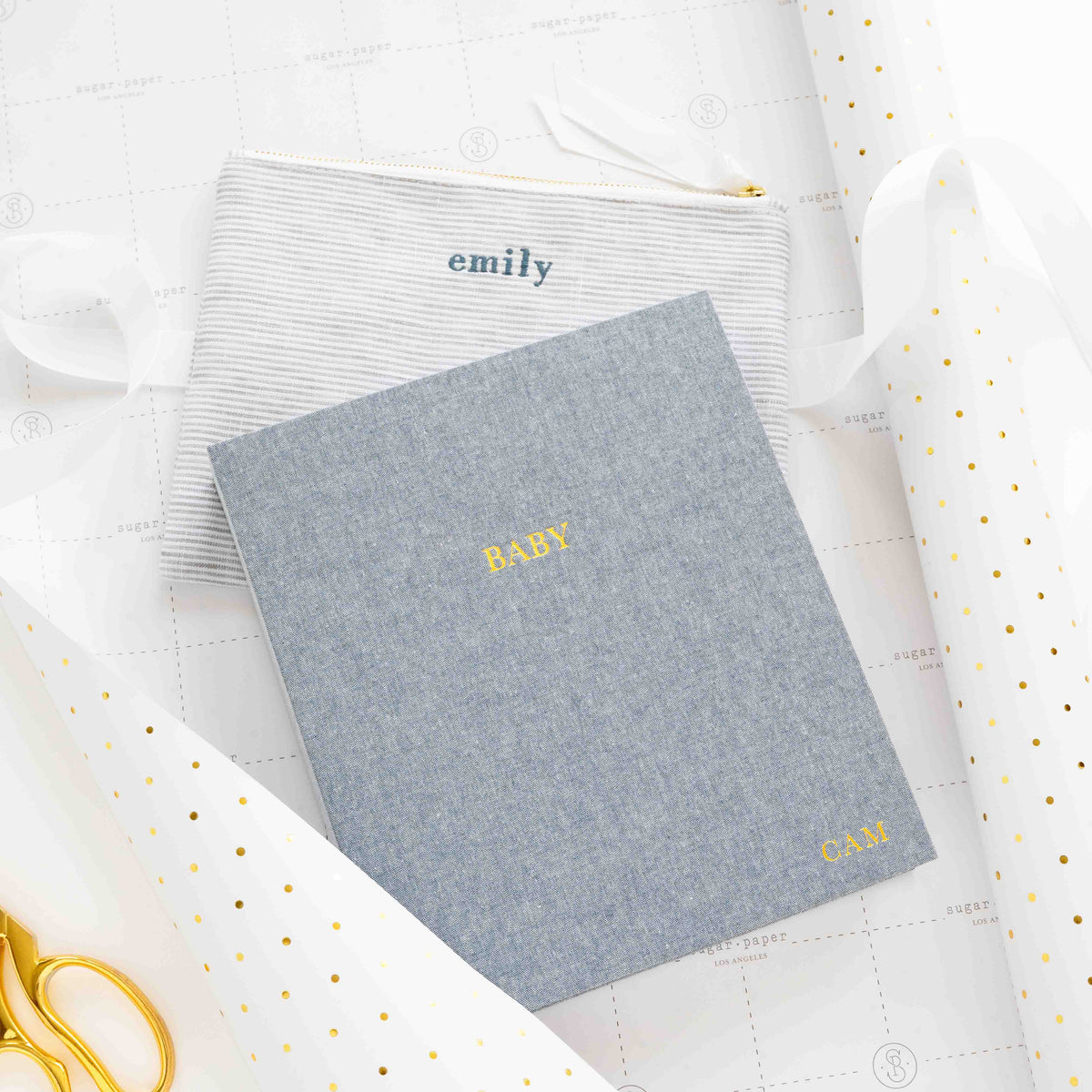 A blue baby book with a monogram and a pouch with an embroidered name.