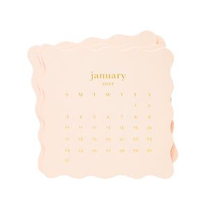 A stack of pale pink paper calendar pages with scalloped edges, showing the month of January 2027 in gold lettering