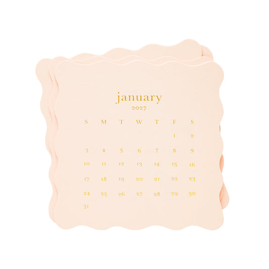 A stack of pale pink paper calendar pages with scalloped edges, showing the month of January 2027 in gold lettering