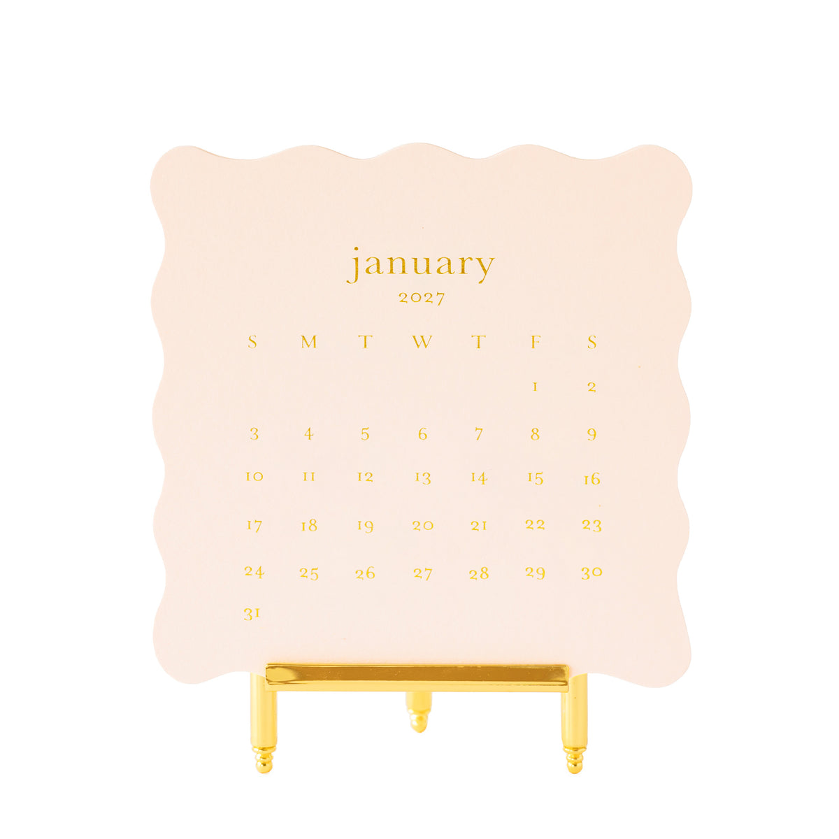 A January 2027 desk calendar on pale pink scallop edge paper with gold foil lettering, displayed on a gold metal easel stand
