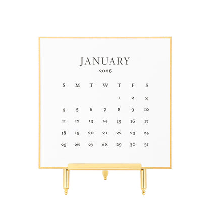 White calendar card with black letterpress ink for January 2026 on a brass stand