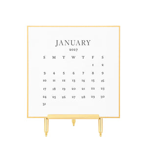 A gold hand painted bordered January 2027 desk calendar with black letterpress ink printed numbers displayed on a gold stand