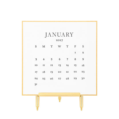 A gold hand painted bordered January 2027 desk calendar with black letterpress ink printed numbers displayed on a gold stand