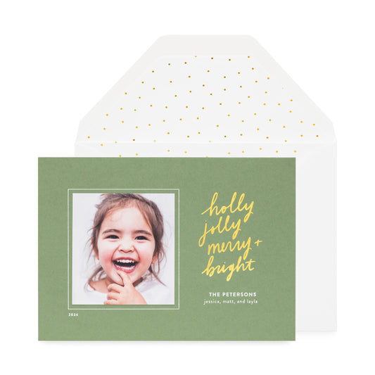 moss green holiday photo card printed with holly jolly merry bright in gold foil paired with a white envelope