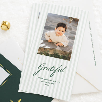 Close up of mint green striped custom holiday photo card with little boy and pine green printed 'grateful this season and always' paired with a white envelope
