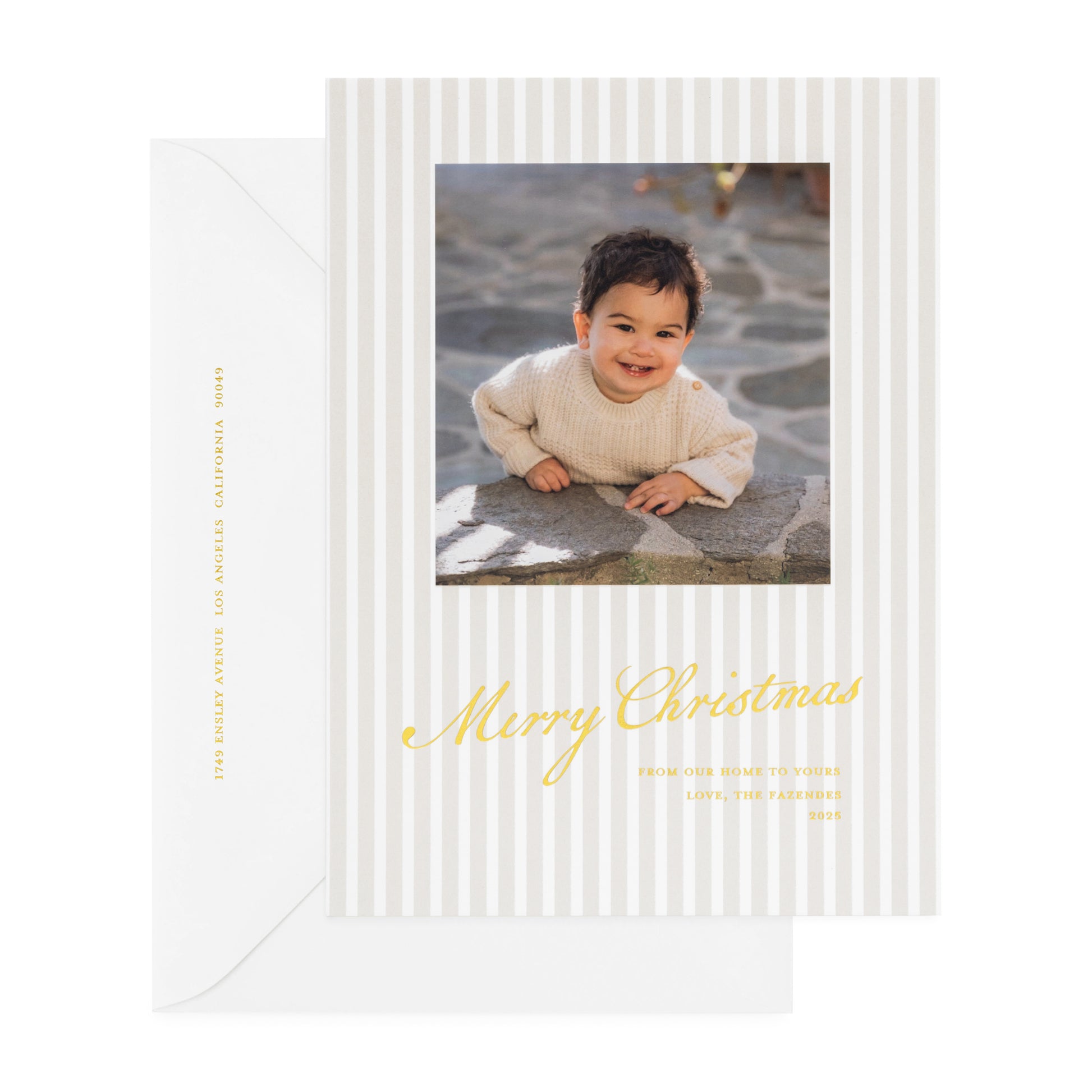 Beige stripe oversized custom holiday card with gold foil 'merry christmas from our home to yours' with photo of little boy paired with a white envelope with gold foil return address