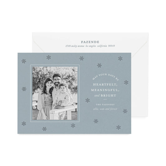 Coastal blue custom holiday photo card paired with a black and white photo with white foil greeting 'may your days be heartfelt, meaningful, and bright' with dark blue snowflake pattern letterpress printed paired with a white envelope with dark blue return address