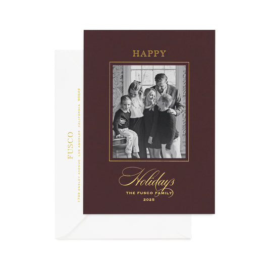 Garnet dark red custom holiday photo card with black and white photo and gold foil greeting 'happy holidays the fusco family 2025' paired with a white envelope with gold foil address