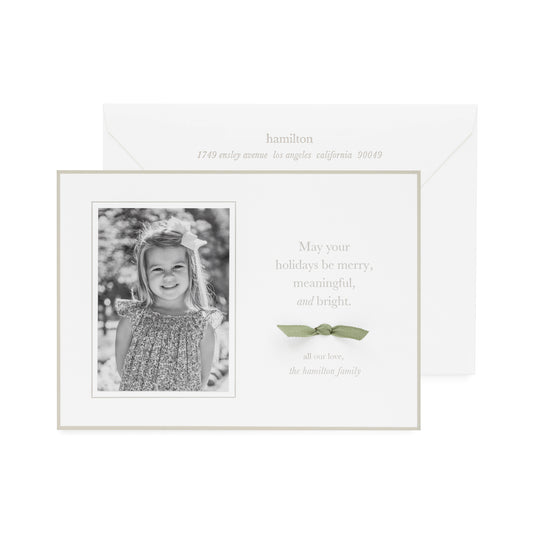 Holiday photo card with black and white photo with oat tan colored border and oat tan colored letterpress ink and sage green bow
