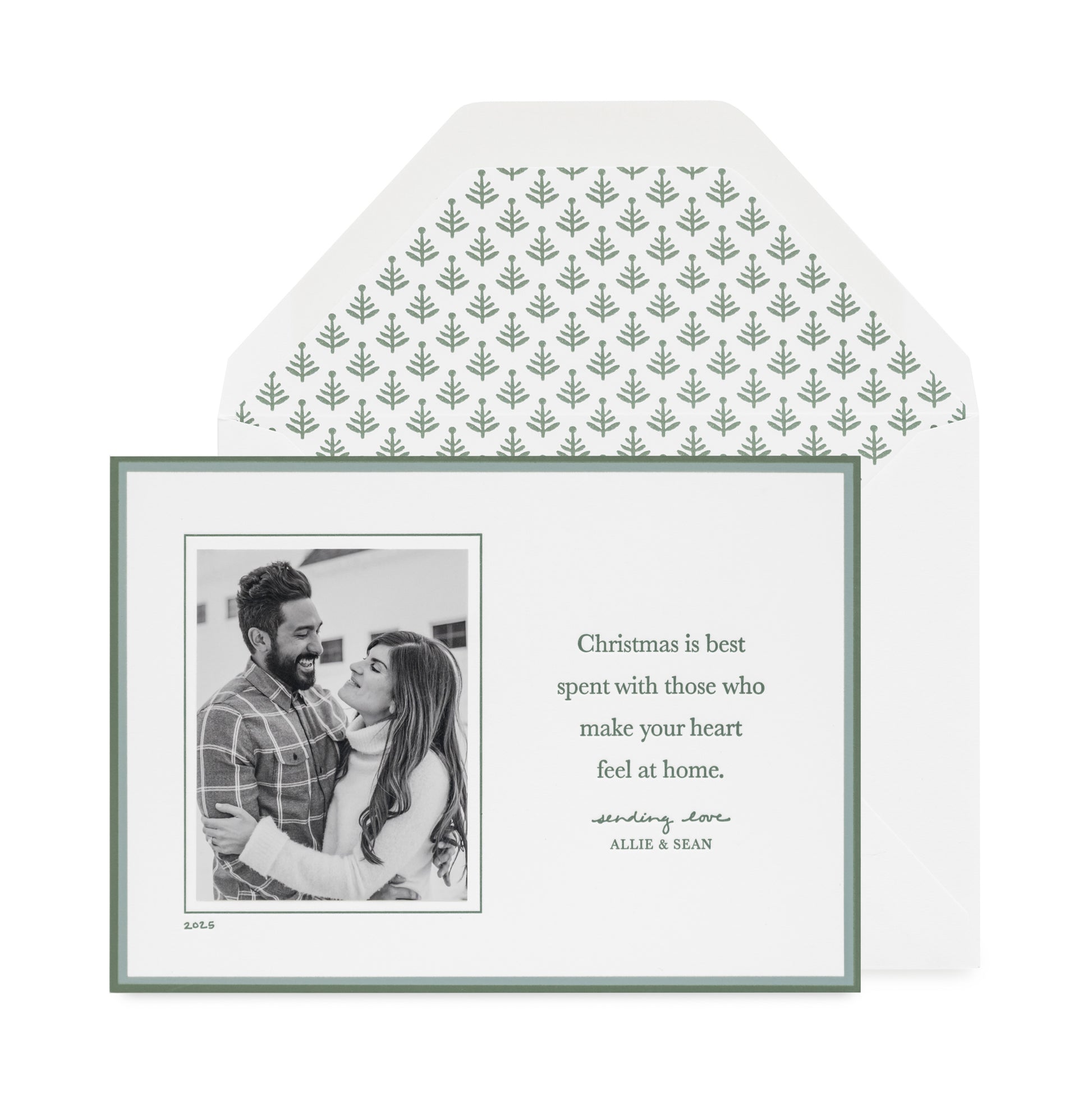 Custom holiday photo card with a black and white photo with a double green border on a white card with green letterpress ink messaging 'christmas is best spent with those that make your heart feel at home' paired with a white envelope with a green tree pattern envelope liner